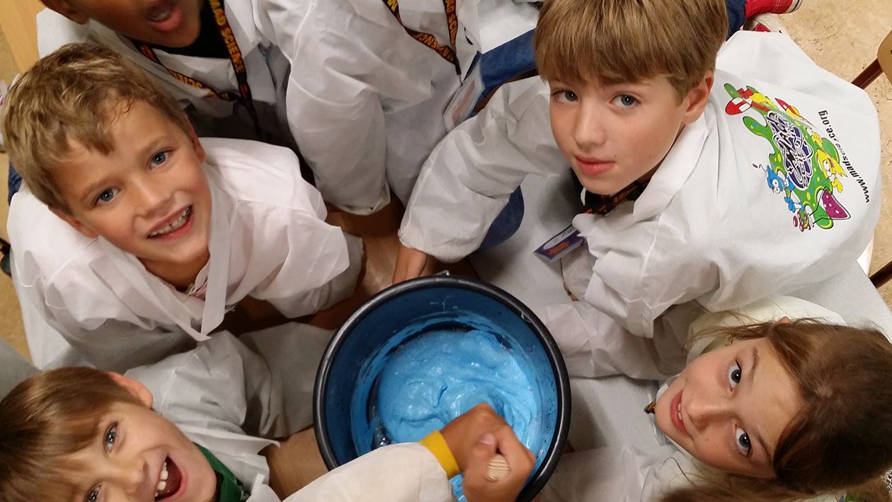 Kids looking up while mixing a big bucket of blue slime