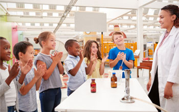 6 kids clapping while teacher finishes science experiment using a Bunsen burner