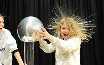 Girl touching a plasma ball causing her hair to to stand up while her mad science instructor looks on.