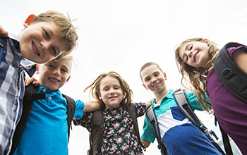 Kids looking down with arms around each all wearing school bags